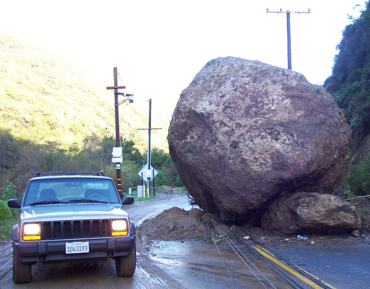 Large rock on roadway dwarfs adjacent vehicle.
