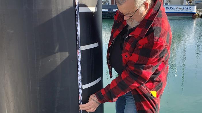 A man measuring tsunami high-water marks on a dock piling.