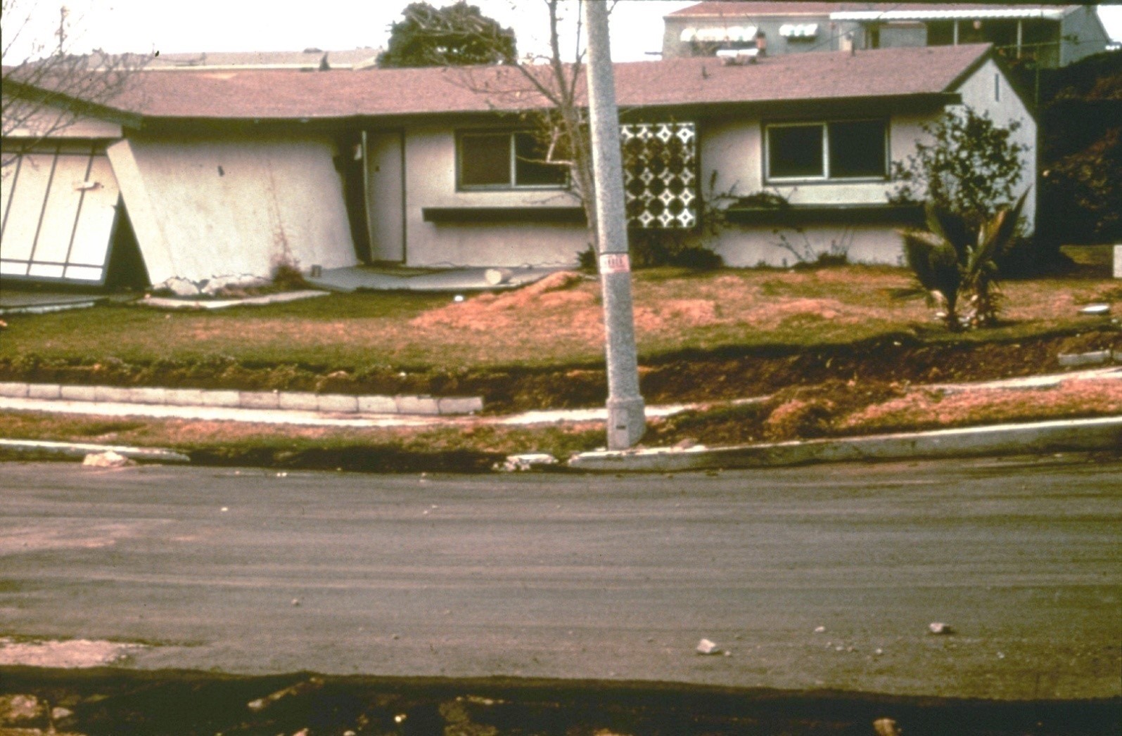 Street view of a partially-collapsed one-story home.